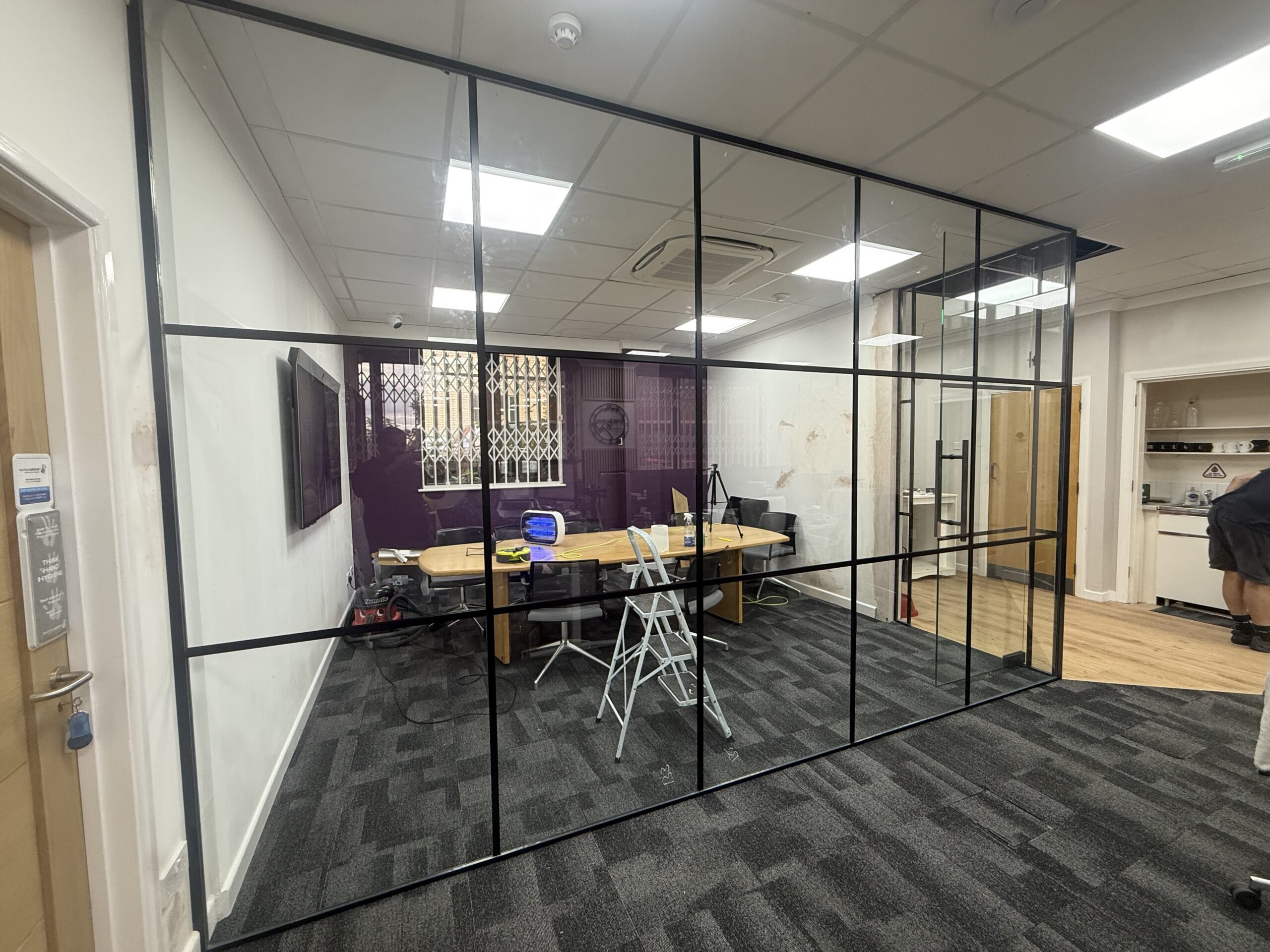 Industrial-style black grid glass partition enclosing a West London office meeting room